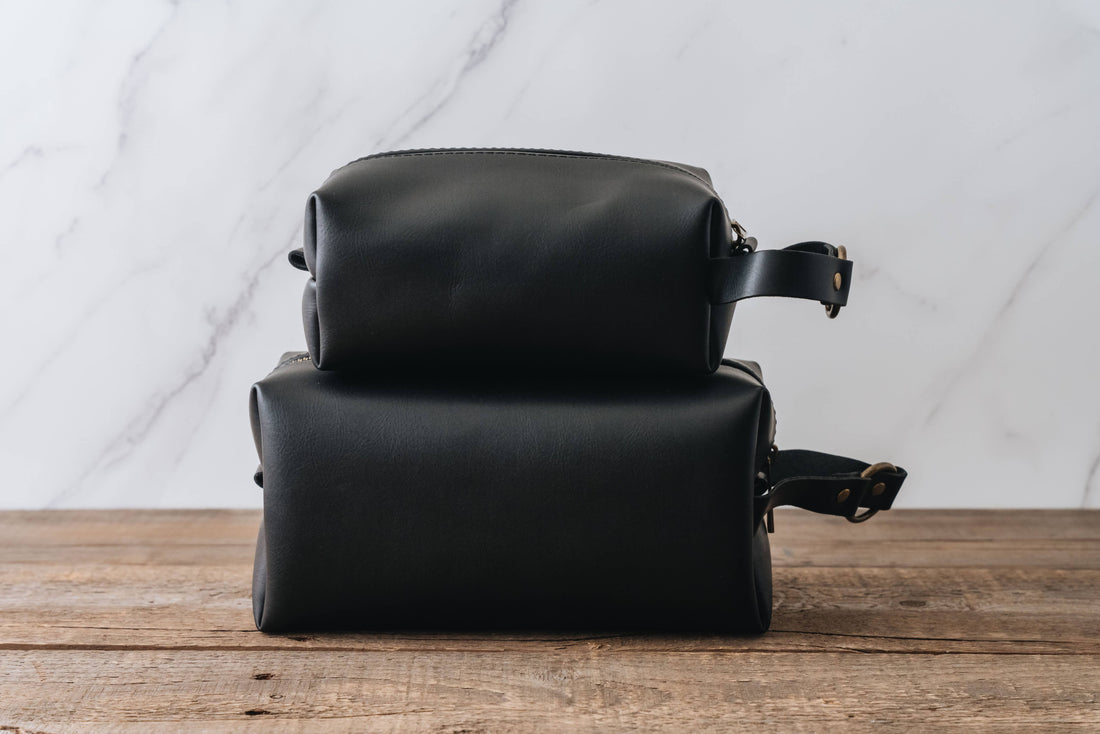 Two black leather bags stacked on a wooden surface with a marble wall background