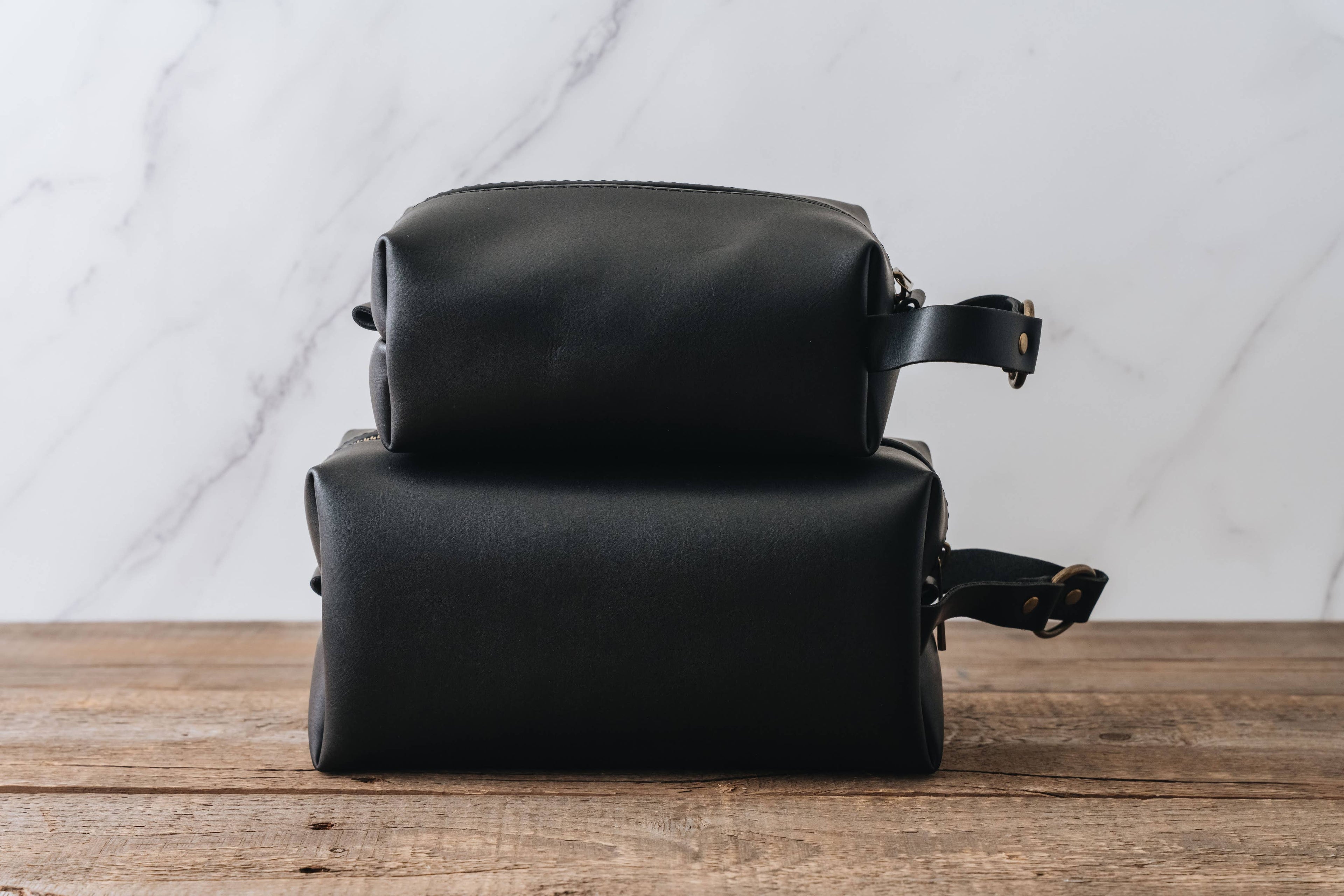 Two black leather bags stacked on a wooden surface with a marble wall background