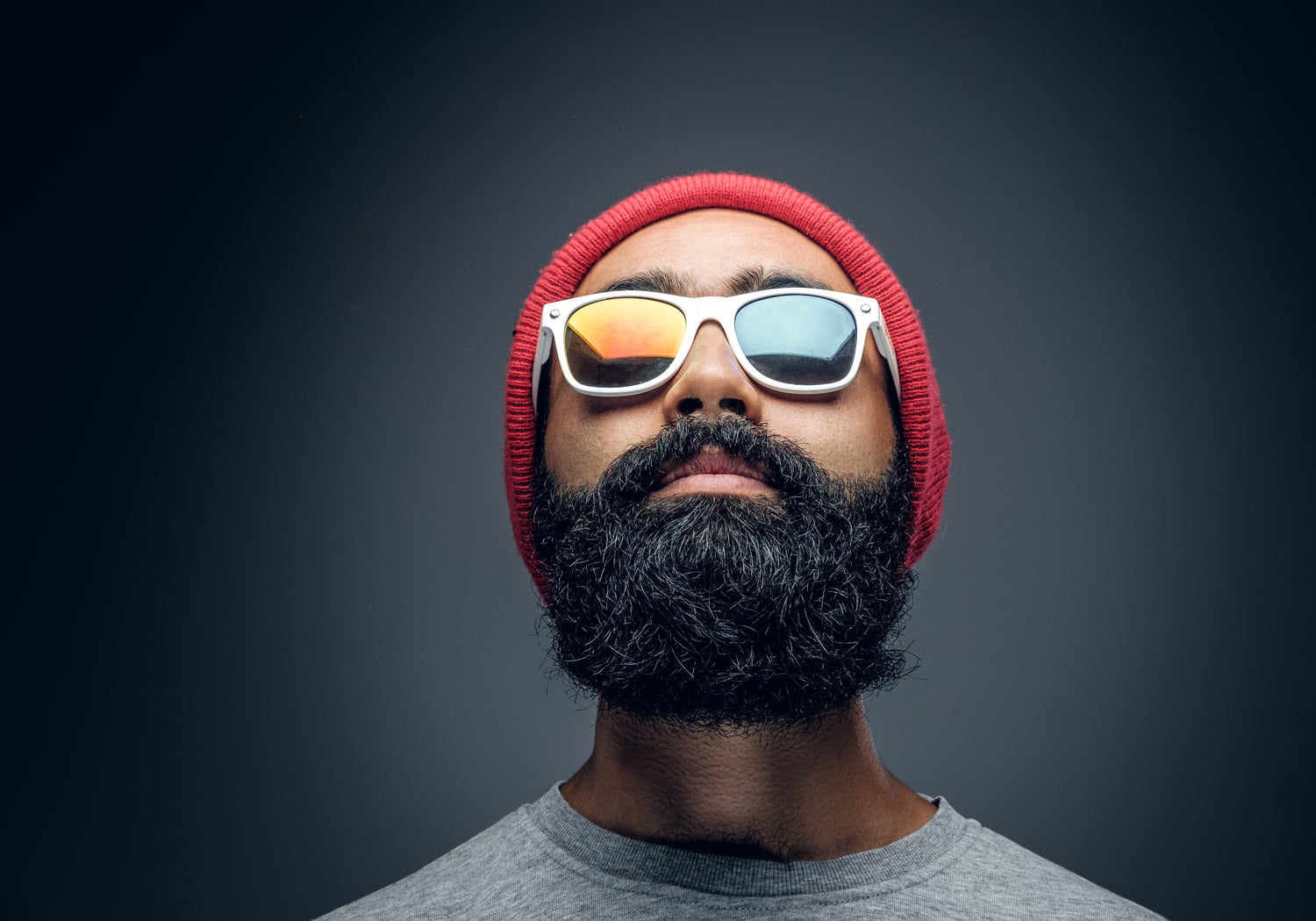 Man wearing a red beanie and reflective sunglasses against a dark background