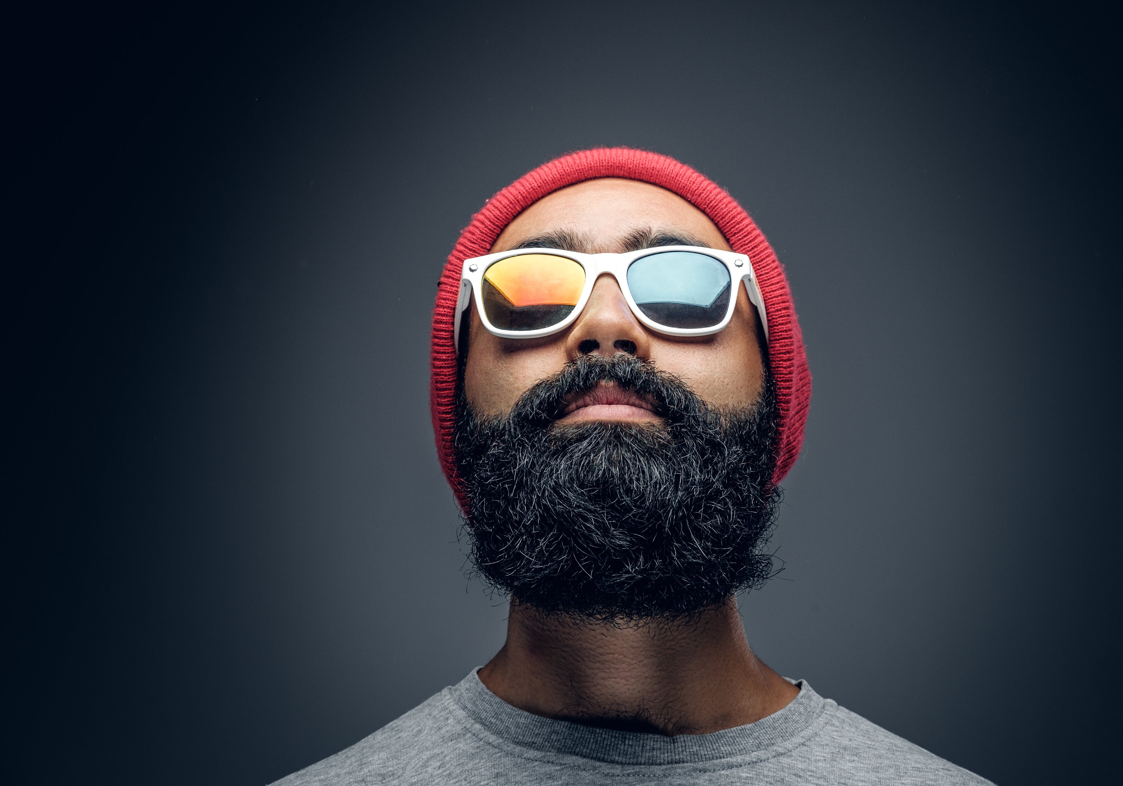 Man wearing a red beanie and reflective sunglasses against a dark background