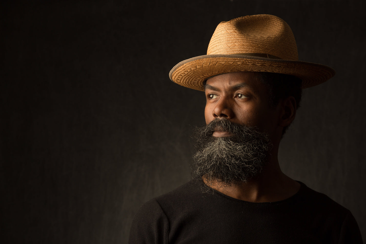 Man wearing a straw hat against a dark background