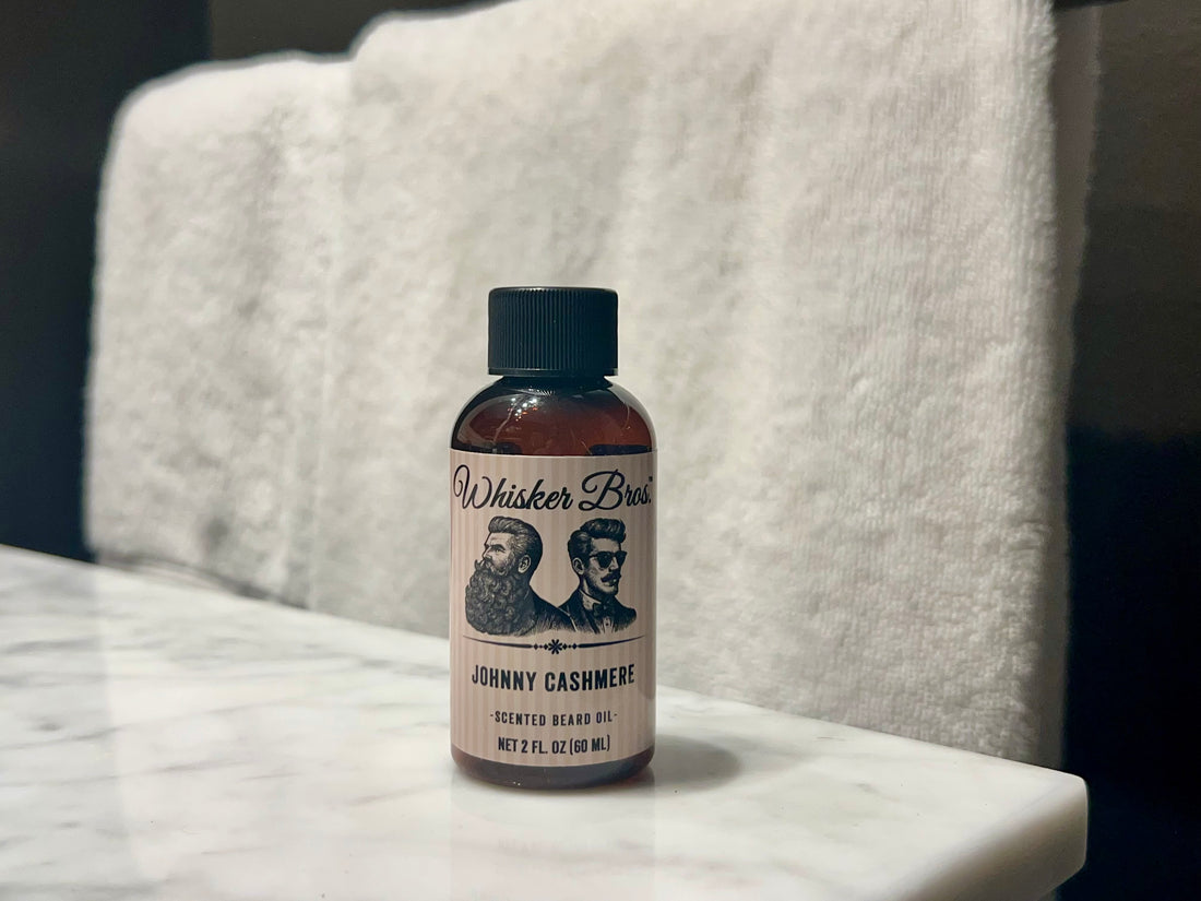 Bottle of Whisker Bros. Johnny Cashmere scented beard oil on a marble surface with a towel in the background.