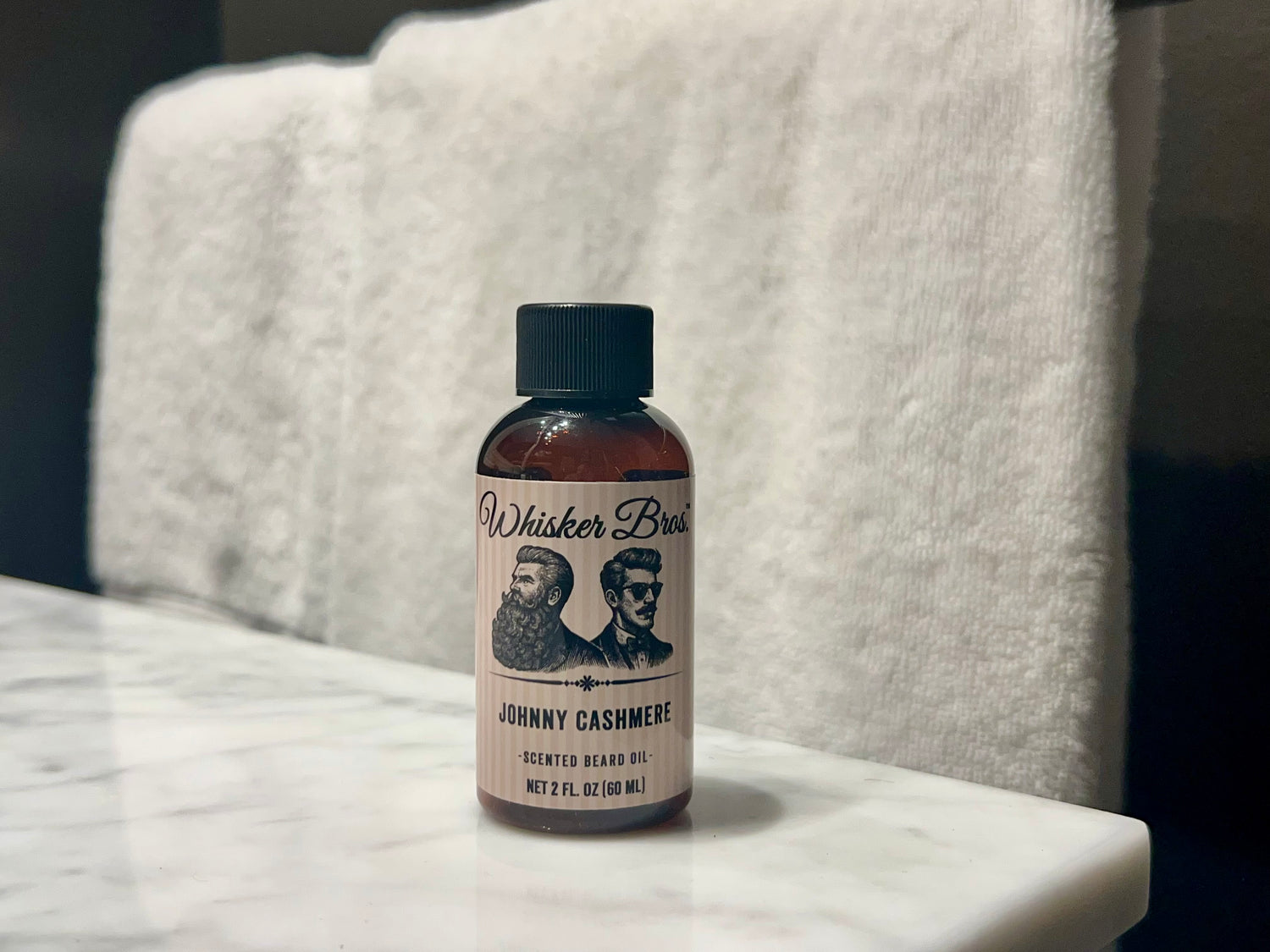 Bottle of Whisker Bros. Johnny Cashmere scented beard oil on a marble surface with a towel in the background.