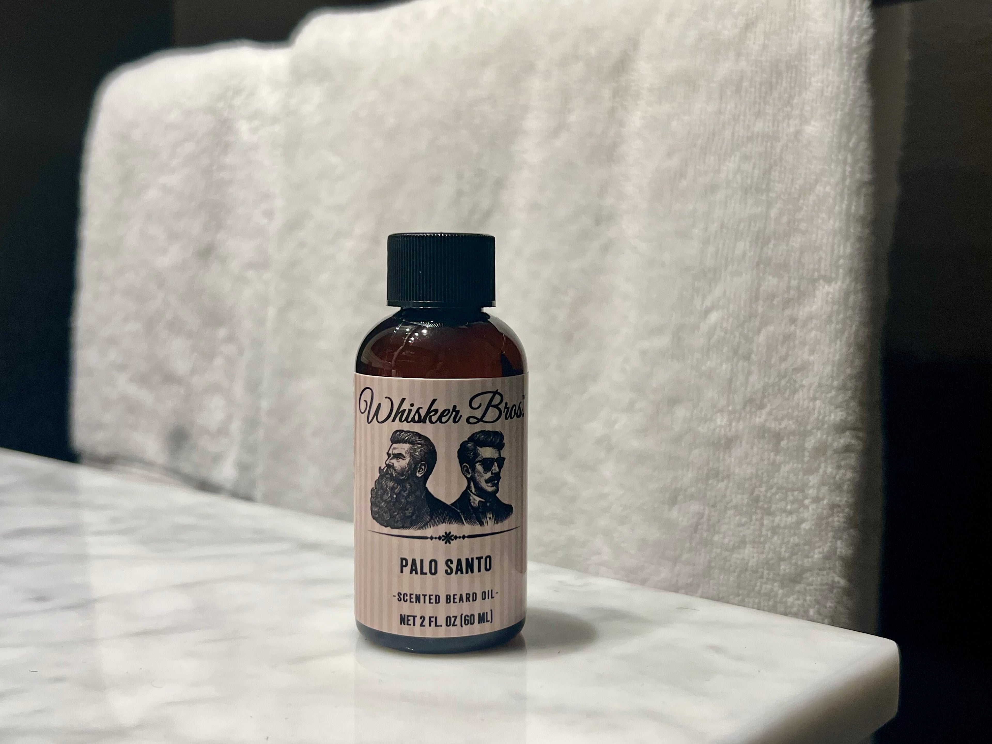 Bottle of Whisker Bros Palo Santo scented beard oil on a marble surface with a white towel in the background.
