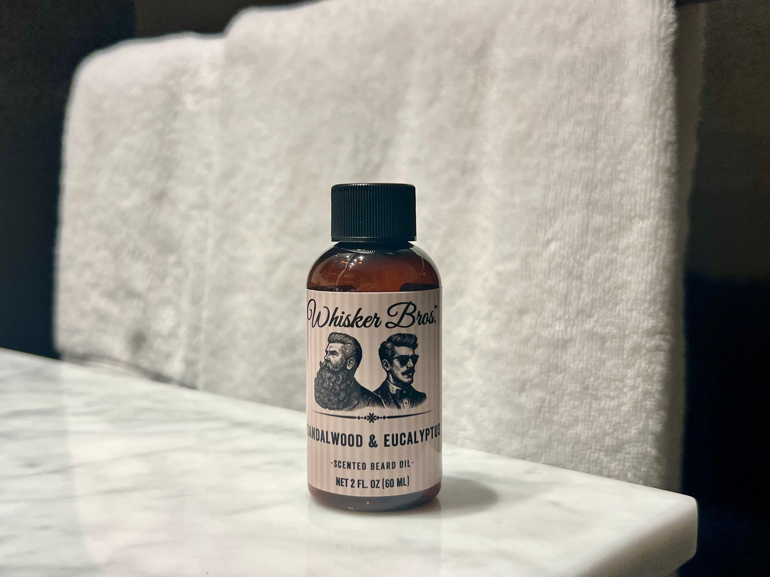 Bottle of Whisker Brand beard oil on a marble surface with a towel in the background