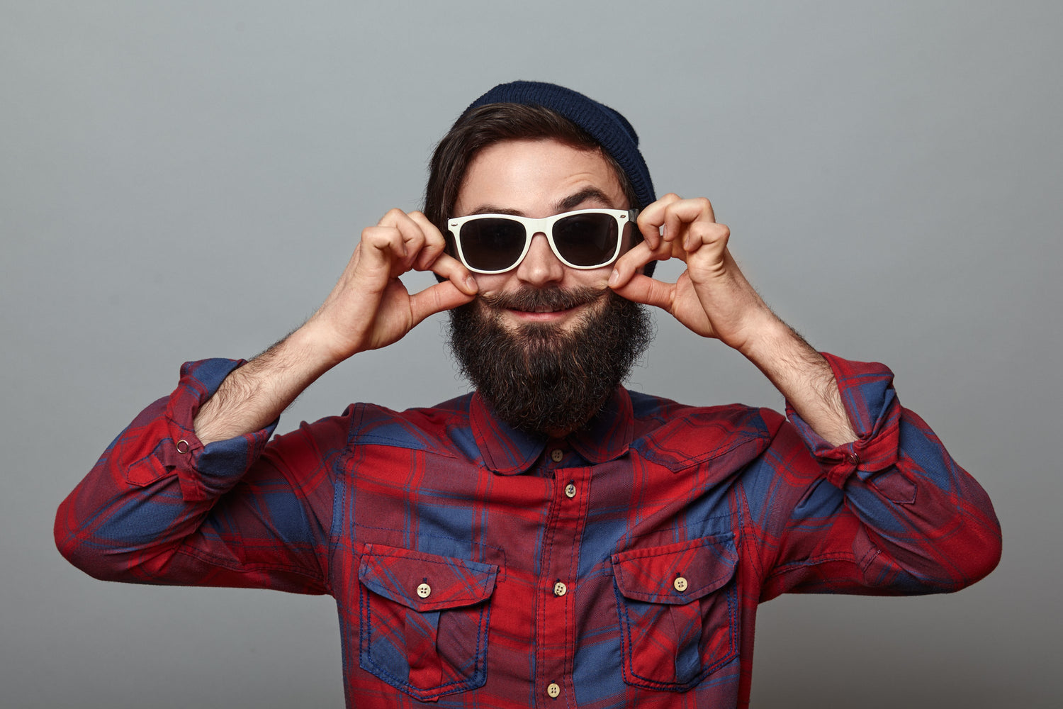 Man wearing a red and blue plaid shirt and sunglasses against a gray background