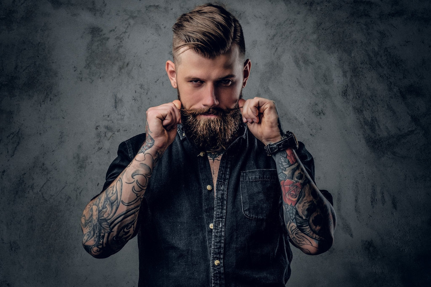 Man with tattoos and a beard holding a leather belt against a dark background