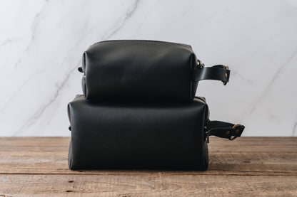 Two black leather bags stacked on a wooden surface with a marble wall background