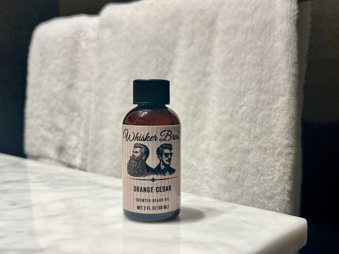 Bottle of Whisker Bros. Orange Cedar beard oil on a marble surface with a white towel in the background.