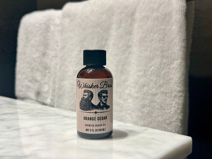 Bottle of Whisker Bros. Orange Cedar beard oil on a marble surface with a white towel in the background.