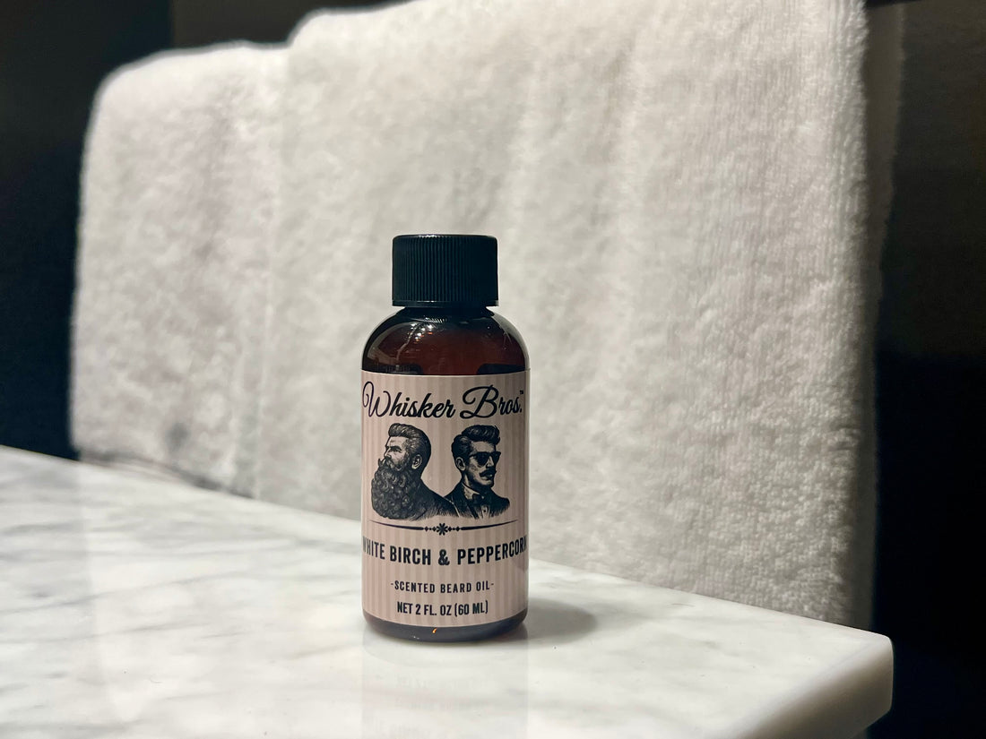 Bottle of Whisker Bros. White Birch & Peppercorn scented beard oil on a marble surface with a white towel in the background.