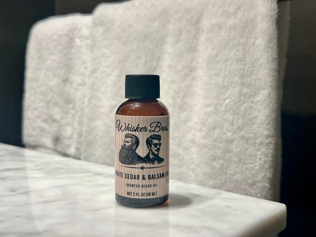 Bottle of Whisker Brand White Cedar & Balsam Beard Oil on a marble surface with a towel in the background.