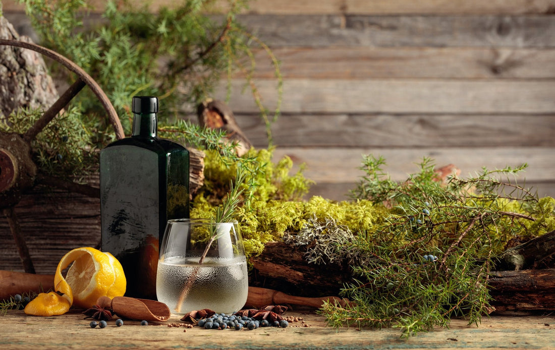 Bottle of gin with a glass of gin and tonic on a rustic wooden surface with herbs and spices.