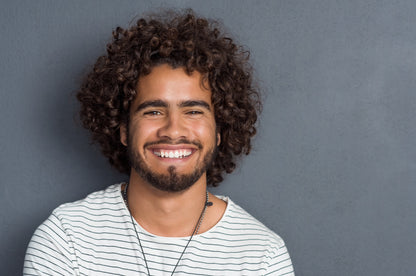 Man with curly hair and a beard wearing a striped shirt against a gray background